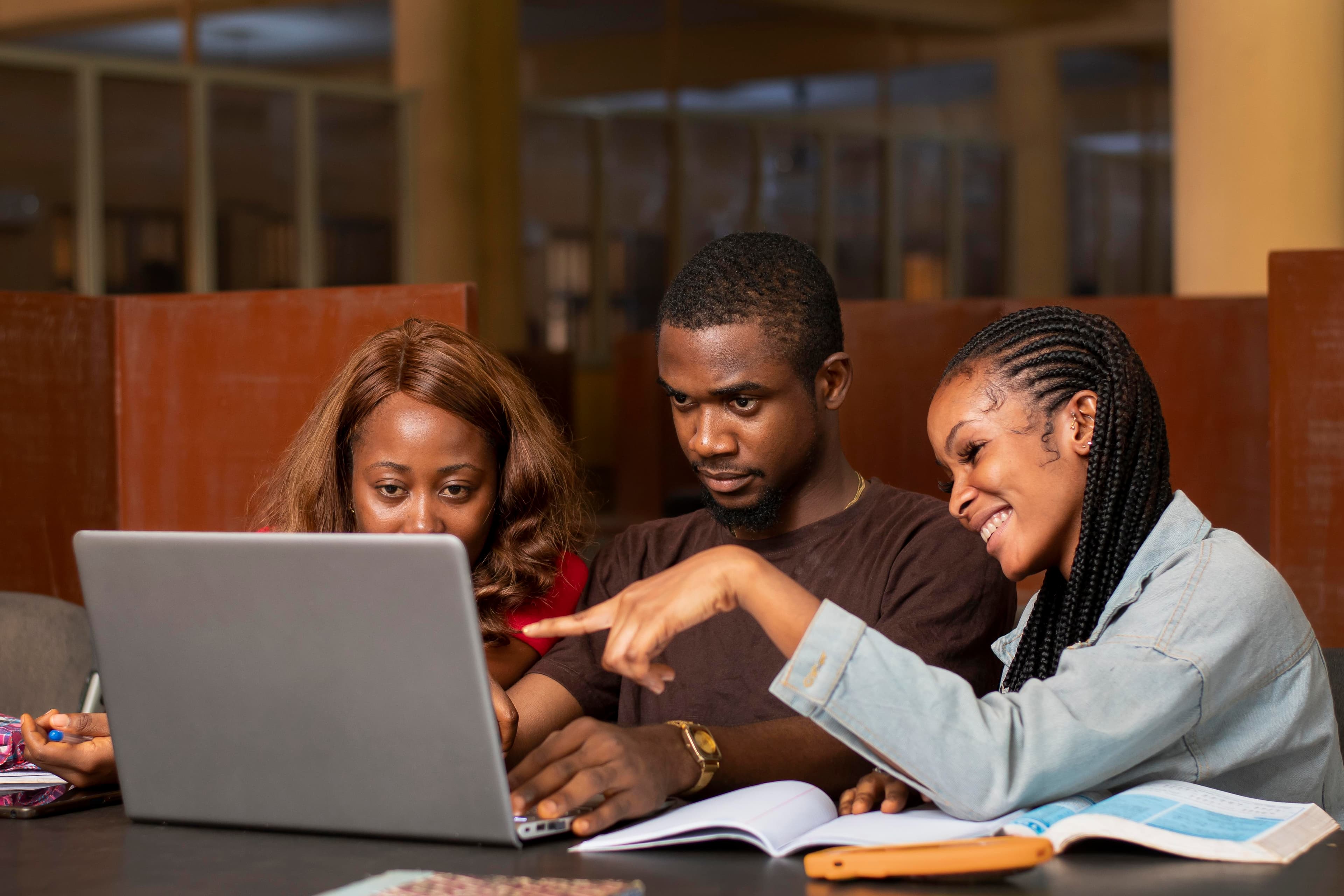 Three learners practicing together around a laptop and notebooks
